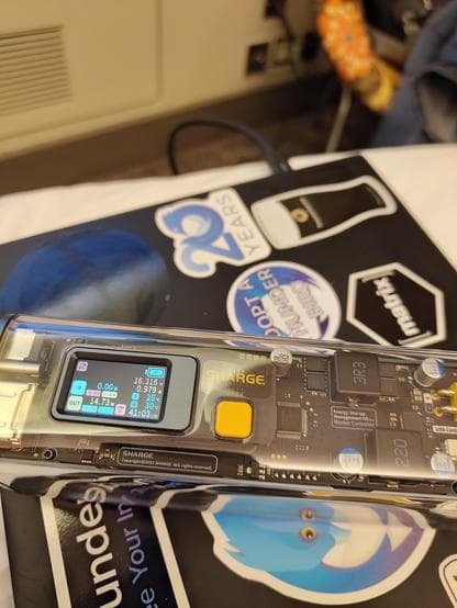 A power bank on a laptop, plugged into a port further forward. It shows an output of about 15W (at 5V).