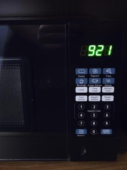 Microwave inside wooden furniture. It has a keypad and quick settings like potato, popcorn, pizza, beverage or frozen dinner on the right. The window in the door is also visible.